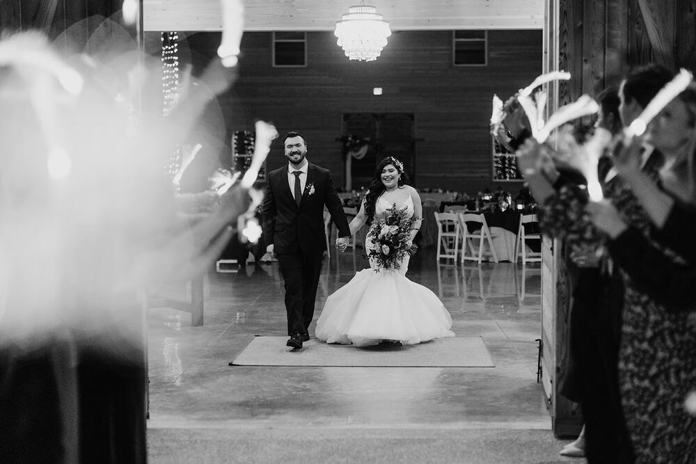 Newlyweds walking into the barn through a tunnel of guests waving light wands