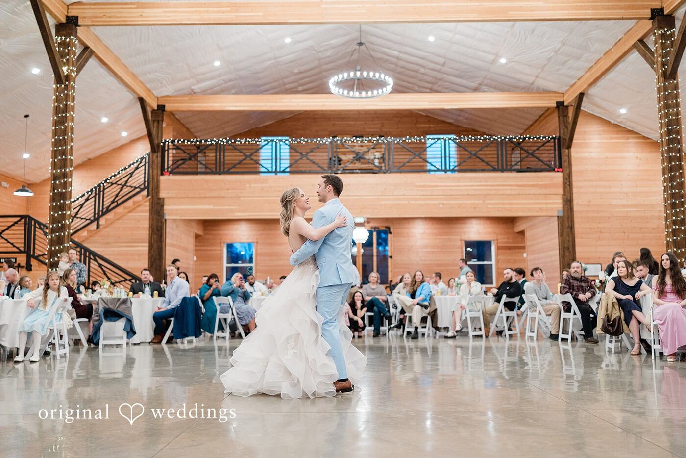 A couple sharing their first dance under the chandelier with the loft behind them