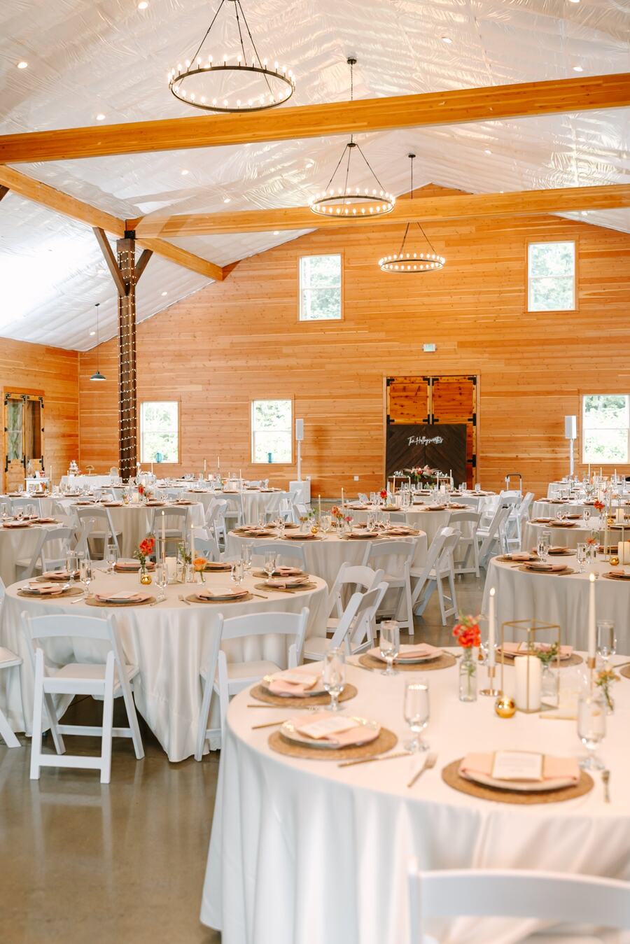 Round tables set with peach napkins and candles under three chandeliers